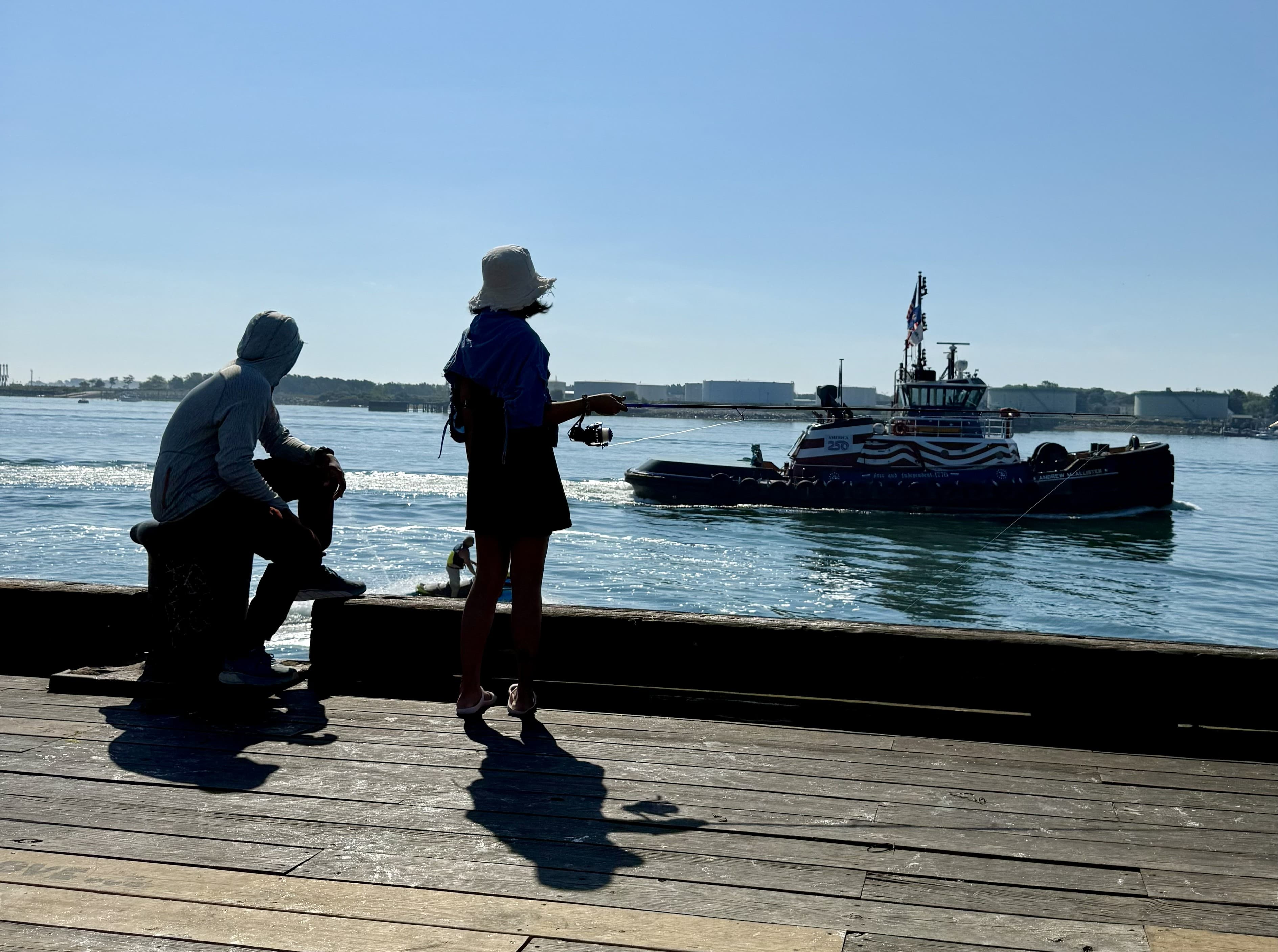 Two anglers standing on pier as jet ski and ferry pass by